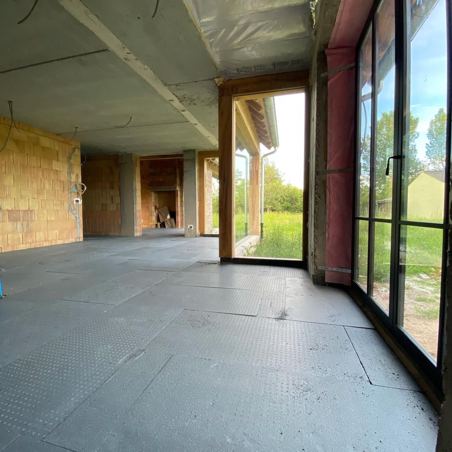 Binnenaanzicht van nieuwbouwproject met geïsoleerde betonnen vloer en glaspartijen, voorzien van vloerisolatie voor energie-efficiëntie.