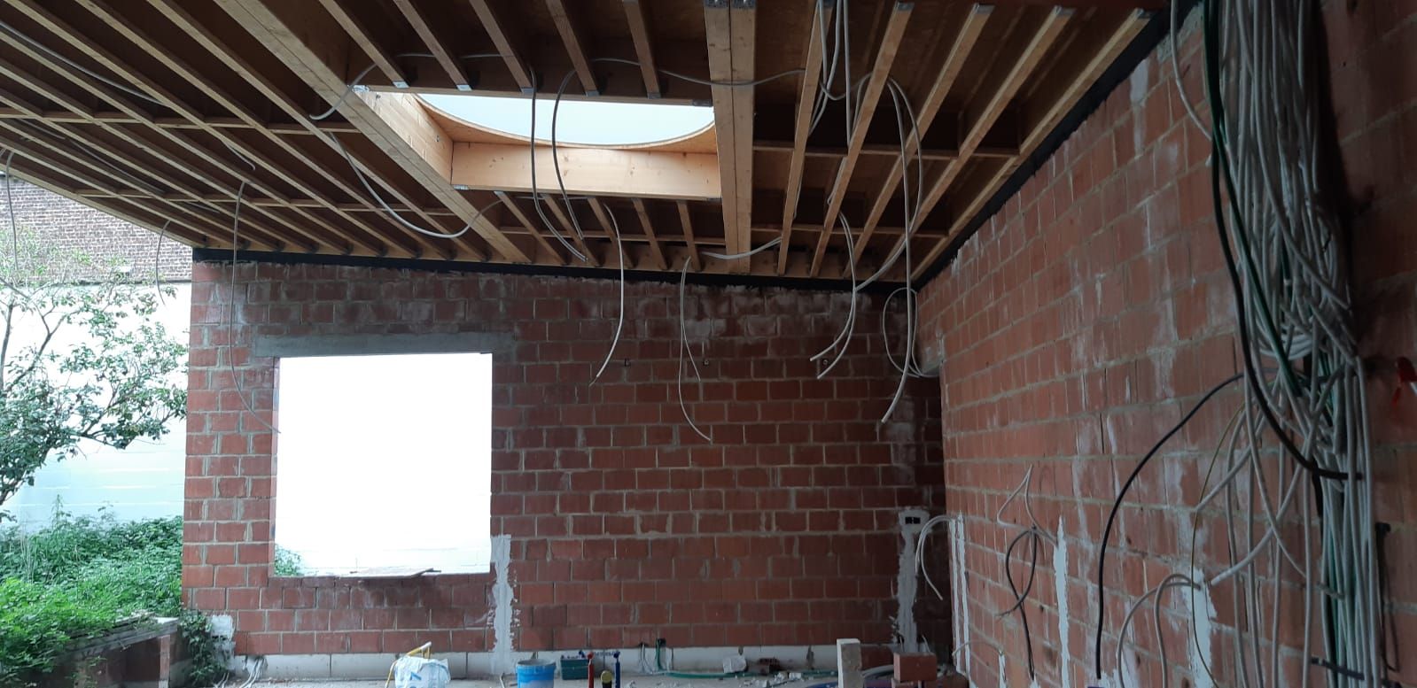 Houten plafond met ingebouwde lichtkoepel, voorbereid voor isolatie en renovatie, zicht op bakstenen muren en bekabeling.